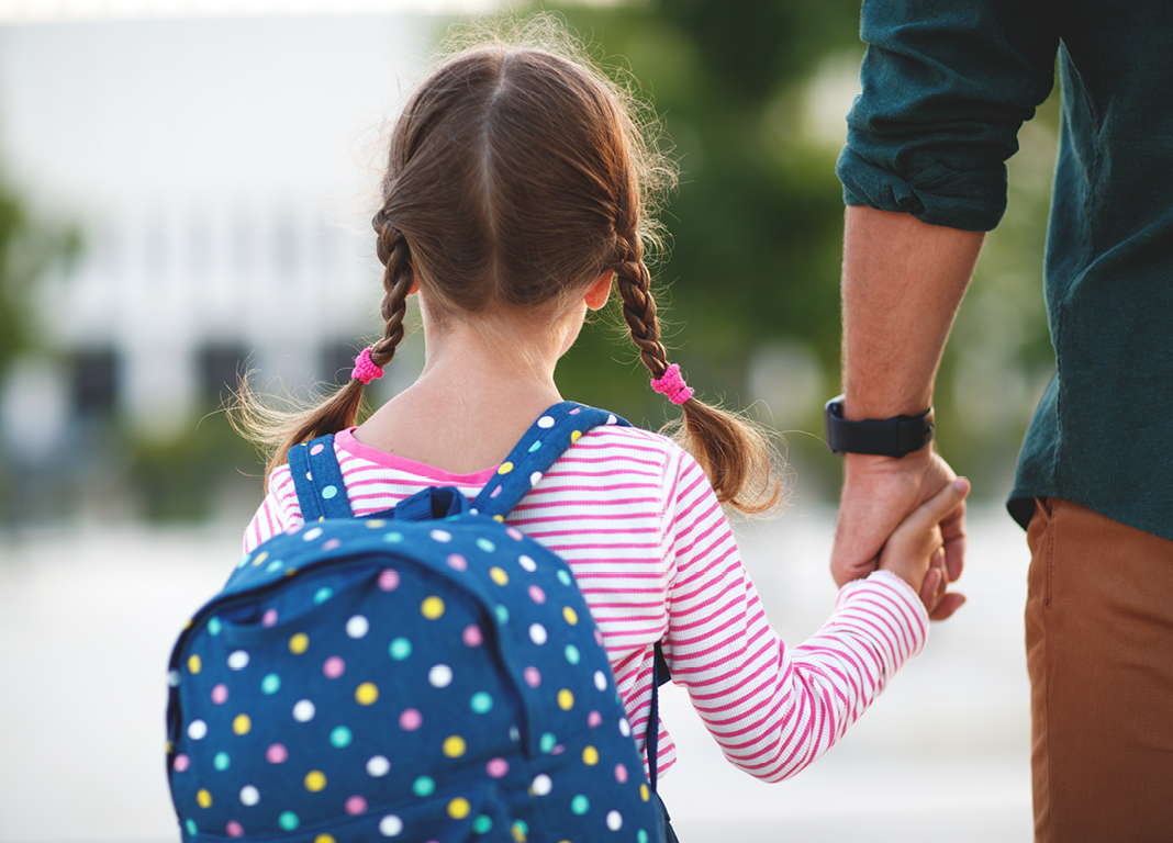 Girl with backpack holding adult's hand 