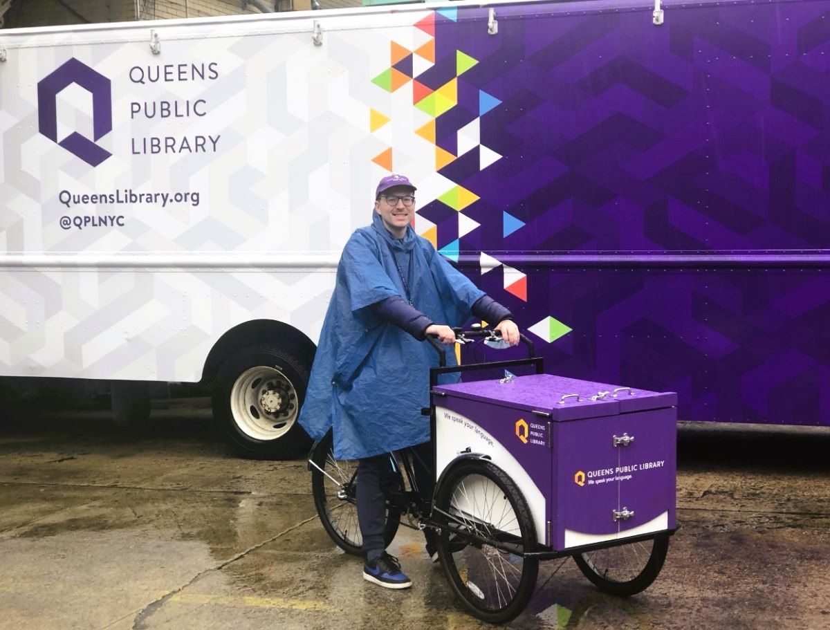 Cambria Heights Library Manager Kacper Jarecki with the QPL Bookbike in front of the QPL Mobile Library.