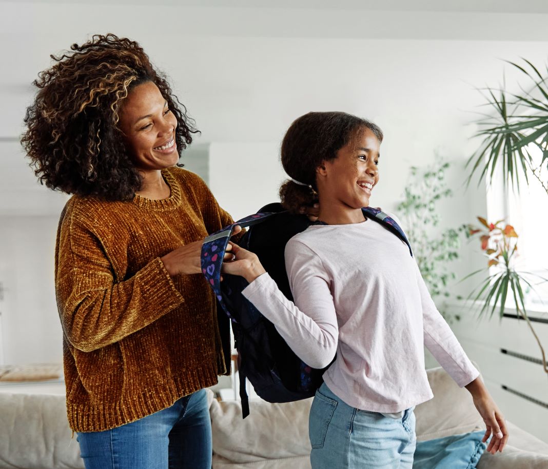 A mother helps her child put on their backpack.